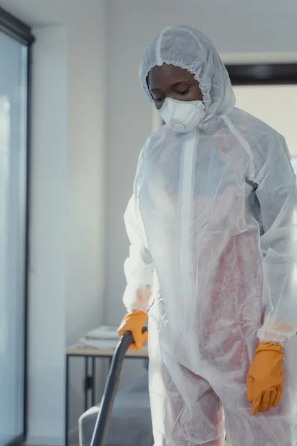 A person in protective gear cleaning a kitchen appliance to ensure hygiene.