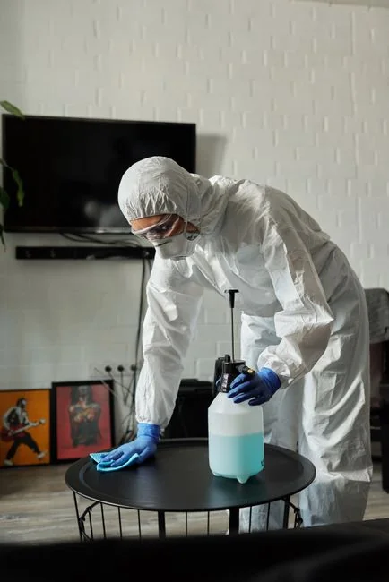Person in protective gear sanitizing kitchen surfaces with disinfectant.